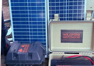 Solar panel array with Wildfire Watchdog wildfire detection and sprinkler system components in Central Oregon. The setup includes roof, eave, and ground sprinklers controlled by ESP32/ESP8266 modules with remote monitoring.